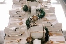 an elegant neutral New Year tablescape with white linens, gold cutlery, gold and gold glitter ornaments, a greenery garland and pillar candles