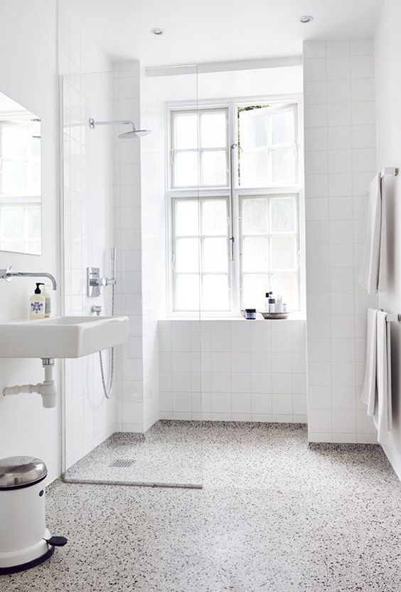 a white airy bathroom is accented with a terrazzo floor of grey, white and black