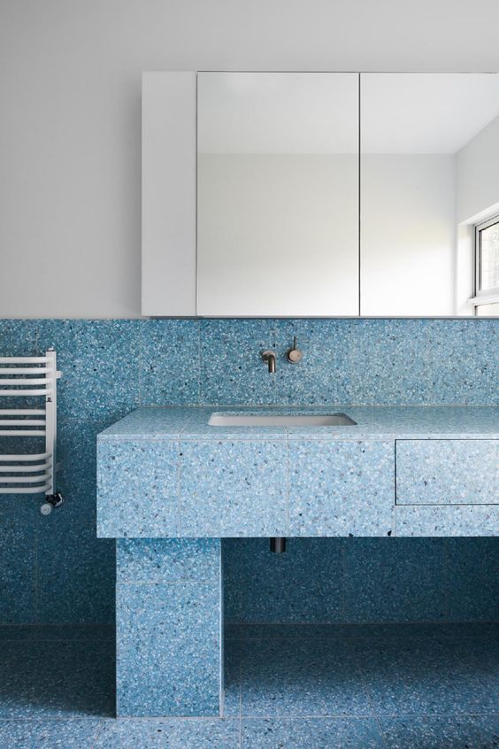 blue terrazzo with navy and white spots covers the walls, floor and the sink stand