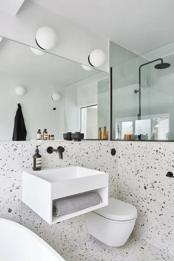 a black and white bathroom with pretty terrazzo, a white vanity and appliances, a shower space and black fixtures
