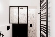a black and white bathroom with white walls, white terrazzo, a black space divider, a white vanity and black fixtures