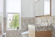 a bold modern bathroom with bright terrazzo tiles, a stained vanity with a terrazzo countertop, a mirror and lamps