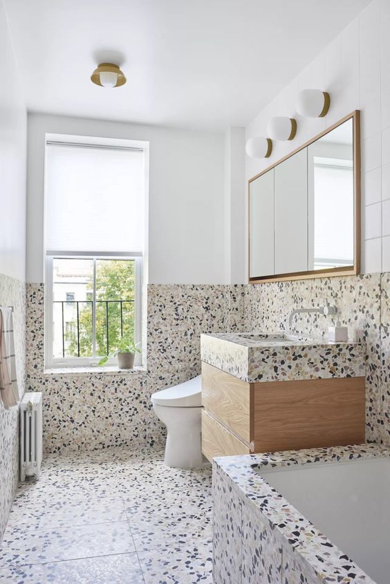 a bold modern bathroom with bright terrazzo tiles, a stained vanity with a terrazzo countertop, a mirror and lamps