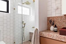 a bold rust-colored bathroom with a shower with a bench, a rust vanity and rust-colored terrazzo on the floor and vanity