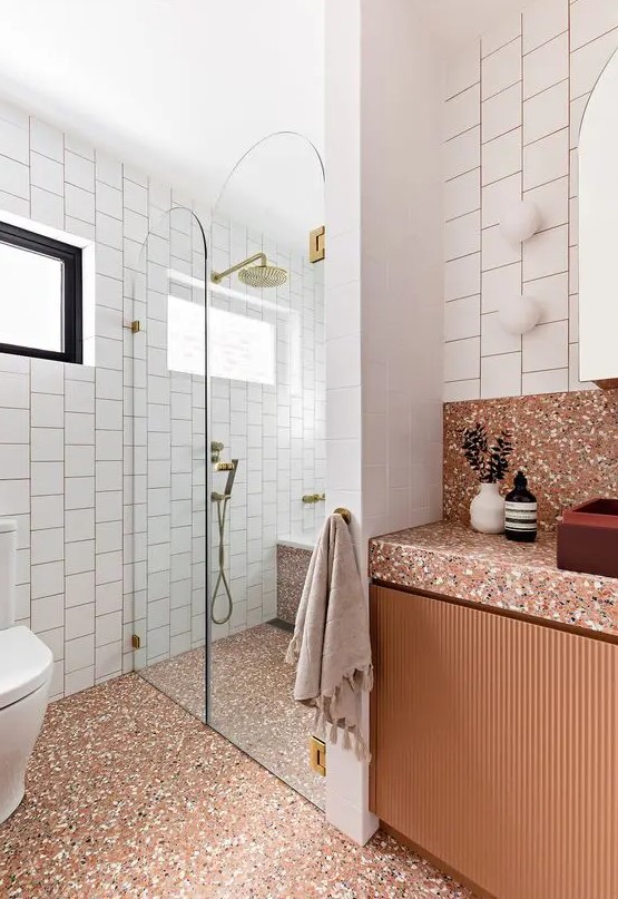 A bold rust colored bathroom with a shower with a bench, a rust vanity and rust colored terrazzo on the floor and vanity