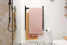 a contemporary bathroom with white tiles, a terrazzo floor, pink tiles, black fixtures and a skylight