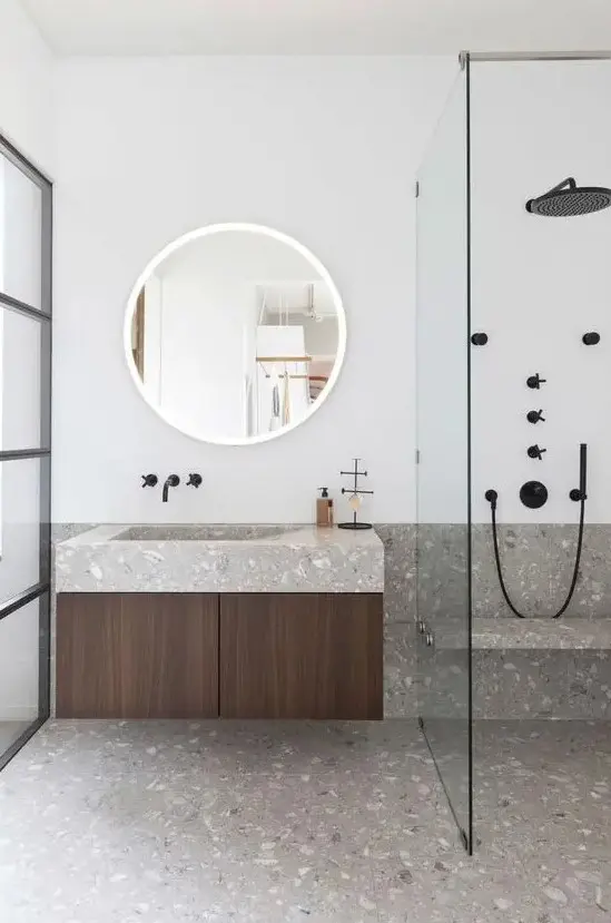 A minimalist bathroom in neutrals is made eye catchy with grey terrazzo on the floor and countertops and black fixtures