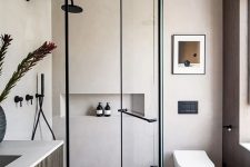 a minimalist bathroom with beige walls, a grey terrazzo floor, a dark-stained vanity, black fixtures and some art