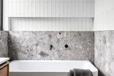 a minimalist neutral bathroom with skinny tiles, grey terrazzo, a tub, a stained vanity is a lovely and eye-catching space