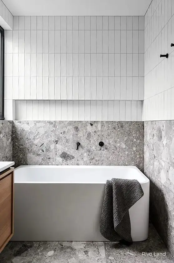 A minimalist neutral bathroom with skinny tiles, grey terrazzo, a tub, a stained vanity is a lovely and eye catching space