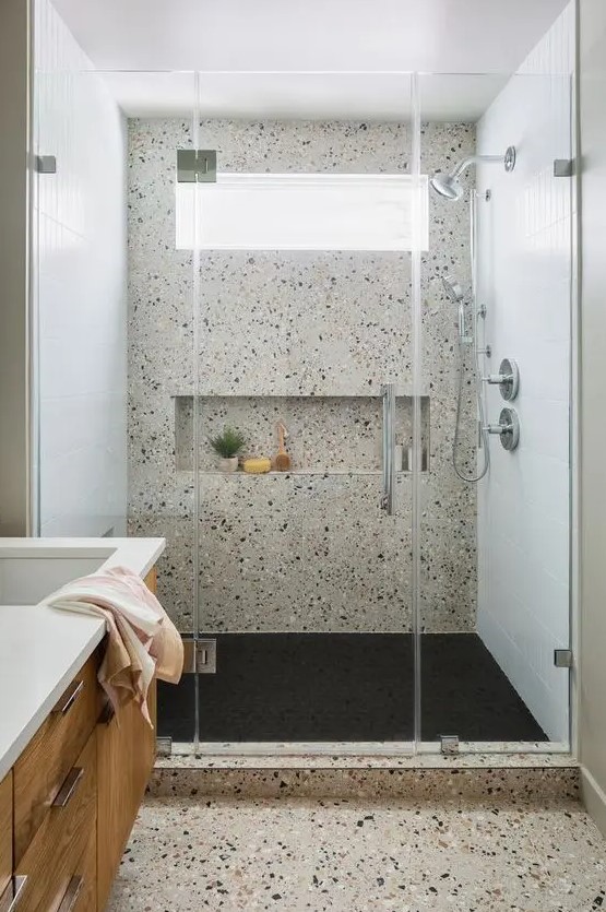 a modern bathroom clad with neutral terrazzo, with a shower space, a stained vanity, a window in the shower for a fresher feel