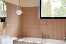 a modern bathroom with dusty pink skinny tiles, blush terrazzo, a white vanity, pendant lamps and a window