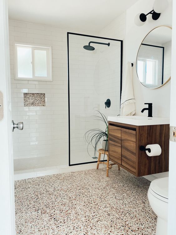 a modern bathroom with white subway tiles and a bright terrazzo floor, a stained vanity, a round mirror and a potted plant