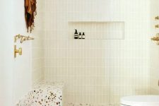 a neutral bathroom with skinny tiles and a bright terrazzo floor, a shower space, a toilet and some gold fixtures