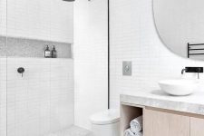 a serene bathroom clad with skinny white tiles, grey terrazzo ones on the floor and a floating vanity and a round mirror