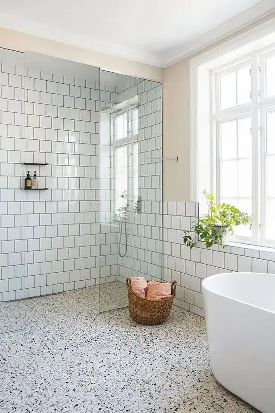 a serene bathroom with white square tiles, a white terrazzo floor for more interest and a white oval bathtub
