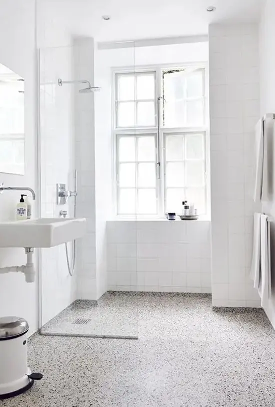 a white airy bathroom is accented with a terrazzo floor of grey, white and black and clad with white square tiles