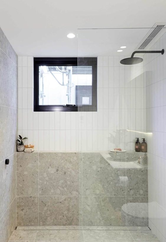 an airy bathroom clad with white skinny tiles and grey terrazzo ones, black fixtures and a window for natural light