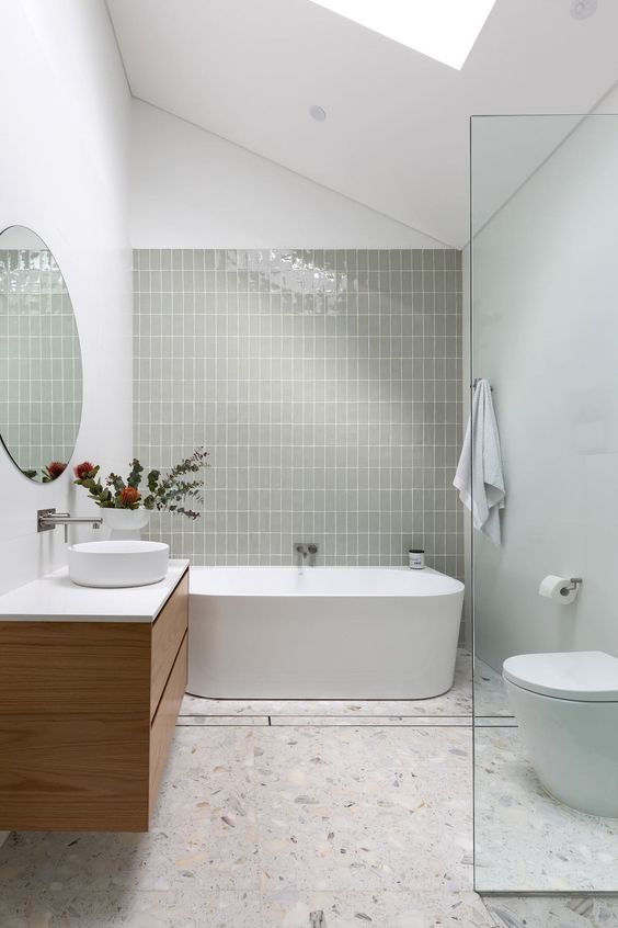 an attic bathroom with an olive green tile wall, a tub, a shower space, a stained vanity, a round mirror and white appliances