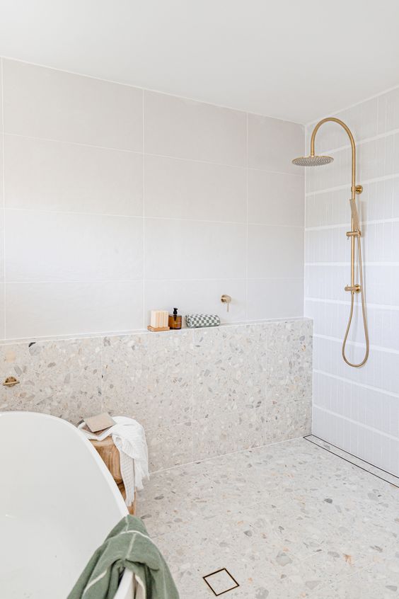 an ethereal bathroom with large scale and white terrazzo tiles, a shower space and an oval tub and brass fixtures