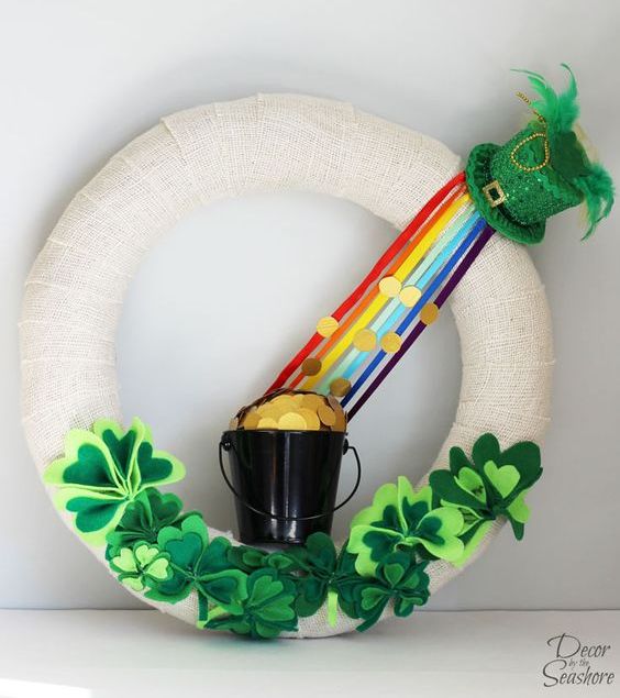 a white burlap wreath with fabric shamrocks, a rainbow and a bucket with gold coins