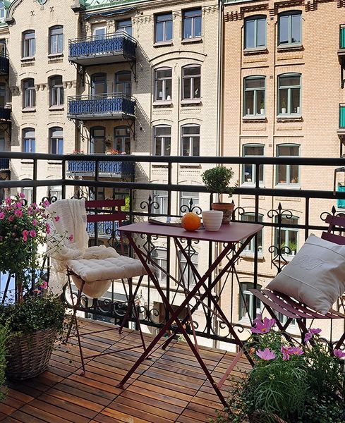 a beautiful and cool balcony with metal folding furniture with pillows, potted blooms and greenery is lovely