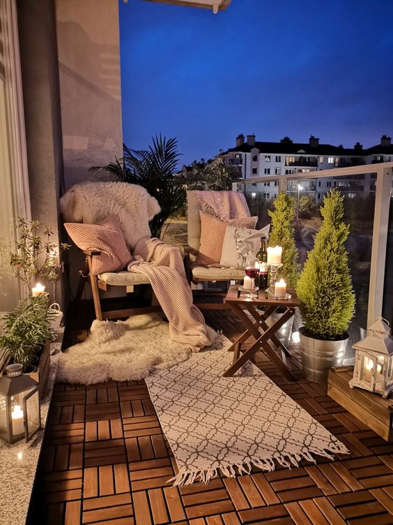 a beautiful balcony with comfortable chairs, a folding stool, a rug, potted plants and candles is a lovely outdoor space