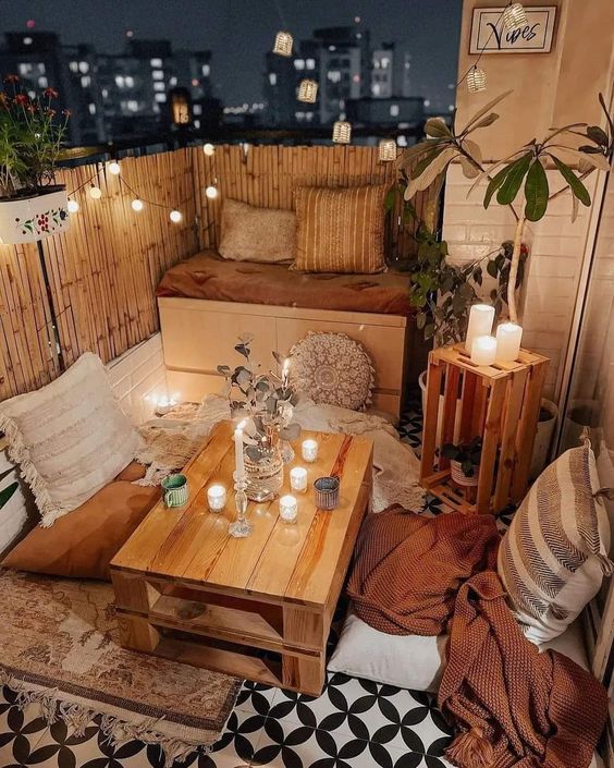 a boho spring balcony with a loveseat, a pallet table and pillows on the floor, candles and lights is a lovely space