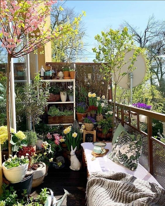 a bright spring balcony with a tiered shelving unit and stools with lots of potted blooms and greenery all around and a bench with pillows