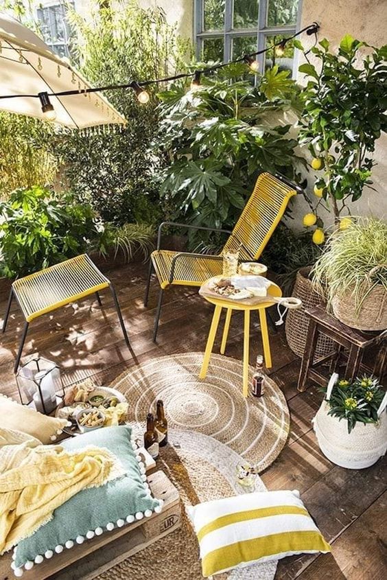 a colorful spring balcony with lots of greenery, blooms, a lemon tree, yellow furniture, rugs and pillows