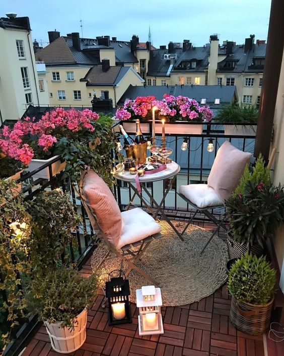 a cozy little balcony with folding chairs and a table, greenery and bright blooms, lights, candles and candle lanterns