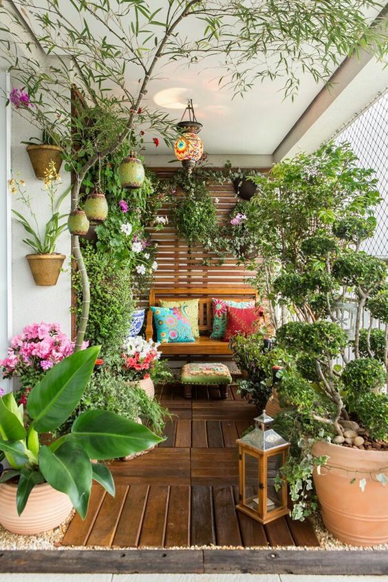 a fantastic colorful spring balcony with a sofa with colorful pillows and a bright stool, potted greenery and blooms and a colorful lamp