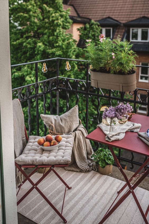 a pretty little balcony with red metal folding furniture, neutral textiles, lights and greenery and blooms is ready for spring