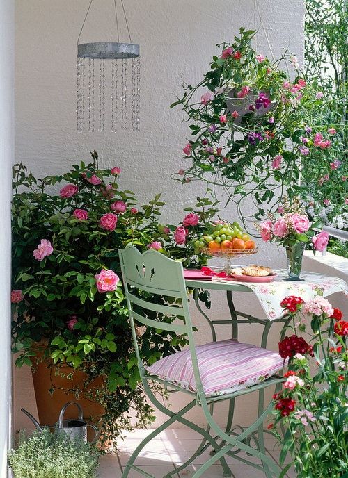 a refined spring balcony with green folding furniture, pink textiles, potted flowers and greenery and a wind catcher