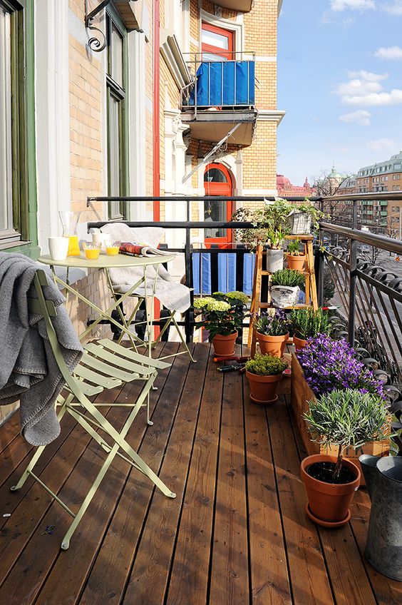 a simple spring balcony with metal folding furniture and blankets, potted greenery and flowers is a lovely space