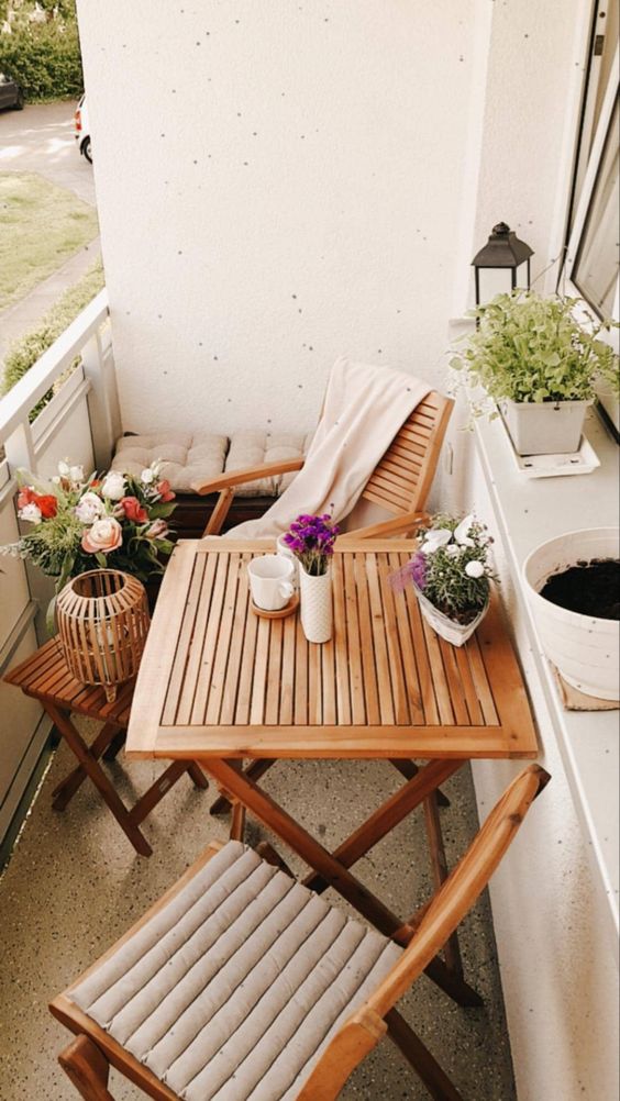 a small and cozy balcony with stained folding furniture, potted blooms, greenery and candle lanterns is wow