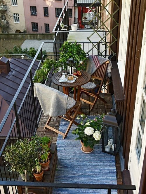 a small and lovely spring balcony with stained folding furniture, potted plants and blooms, candle lanterns and rugs is cool