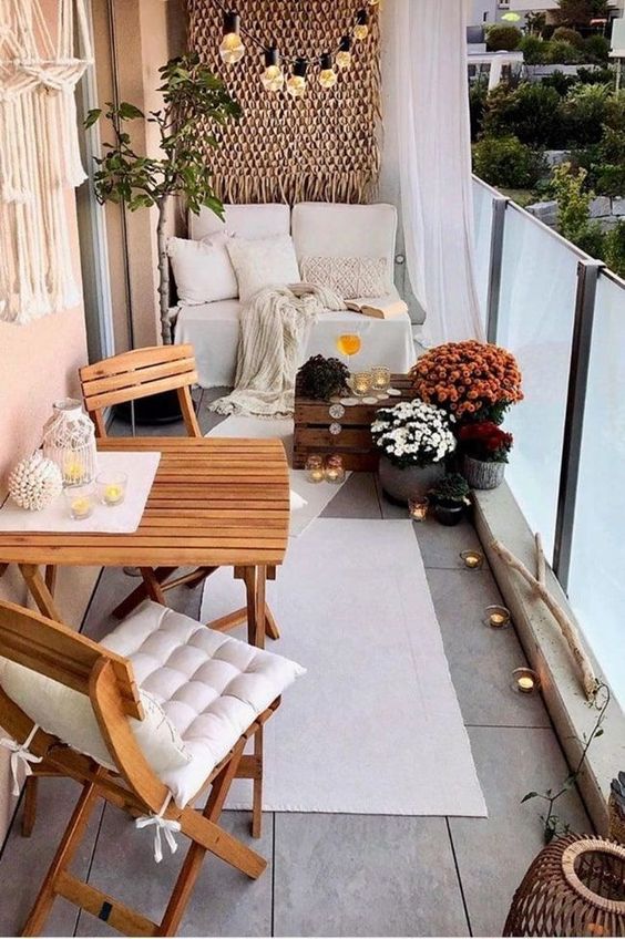 a small and pretty balcony with lights, folding furniture, a sofa with pillows, candles and greenery and blooms