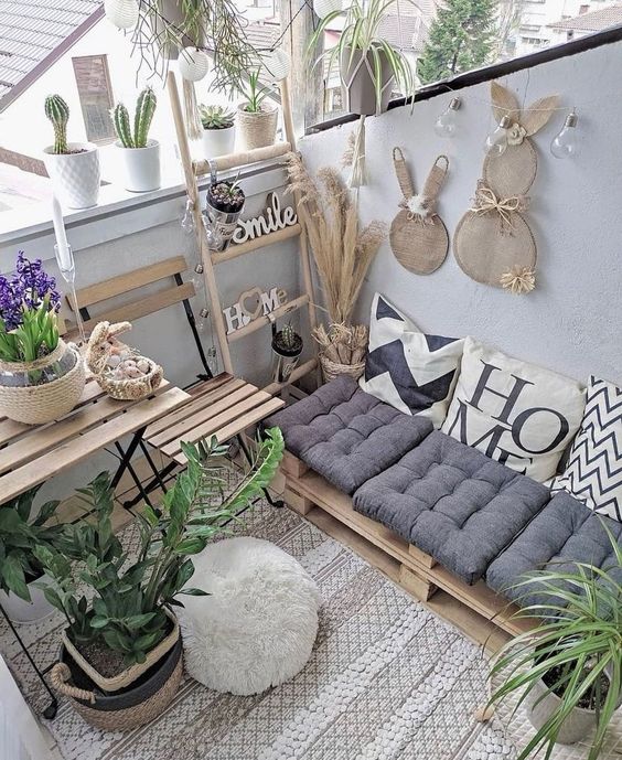 a small boho balcony with folding furniutre, a pallet daybed, pampas grass and bunny decor, some blooms