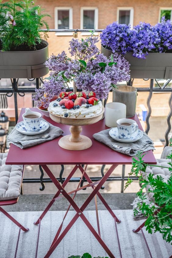 a small spring balcony with vintage red metal folding furniture, some bright blooms and greenery and coffee served