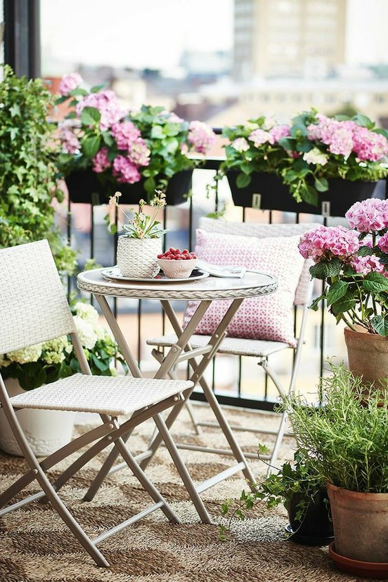 a small spring balcony with white folding furniture, potted greenery and pink flowers and a pink pillow is great