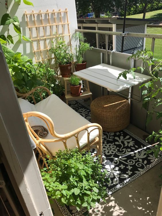 a spring Scandinavian balcony with a wall-mounted table, a rattan loveseat, greenery and a printed rug is a cool space