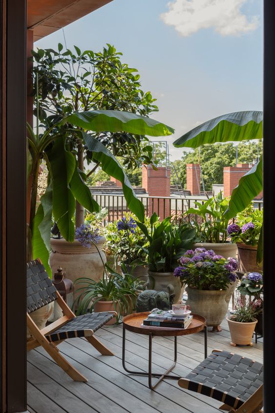 a spring balcony with a folding chair, a side table, potted flowers and greenery is a lovely space for spending time outdoors