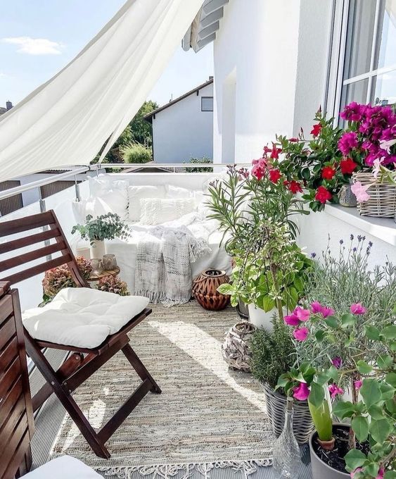 a spring balcony with a white loveseat and pillows, a folding chair, potted plants and bright flowers is wow