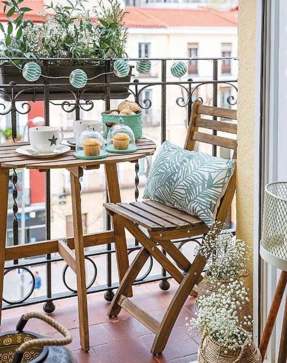 A spring balcony with stained folding furniture, lights, blooms and greeenery and mint colored tableware