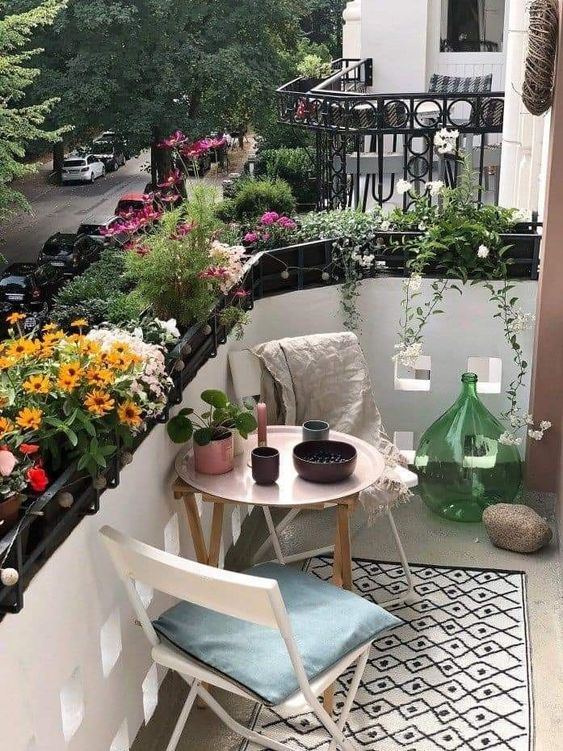 a stylish small balcony with white folding furniture, a printed rug, greenery and colorful flowers and some lovely decor