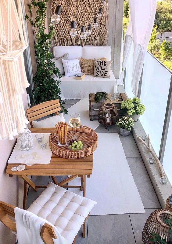 a white balcony with a loveseat and pillows, stained folding furniture, a rug, lanterns and blooms and bulbs hanging