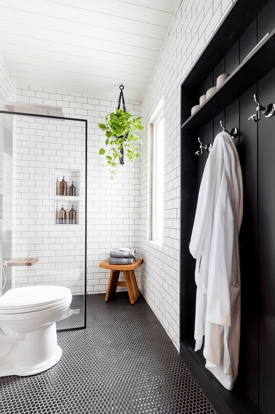 a Nordic bathroom with white subway and black penny tiles, a wooden built-in piece, some greenery and niches in the shower space