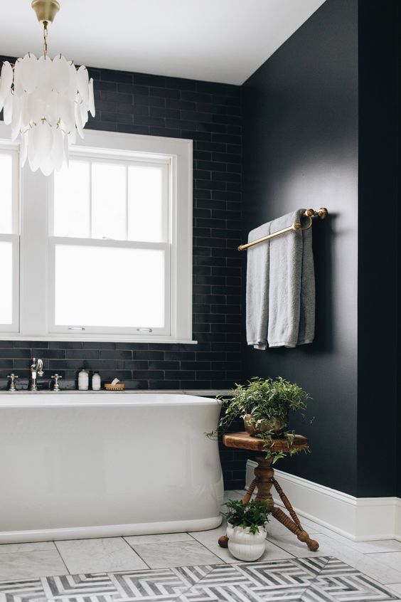 a beautiful and elegant bathroom with black walls and black tiles, a white tub, a black and white tile floor, a mother of pearl chandelier