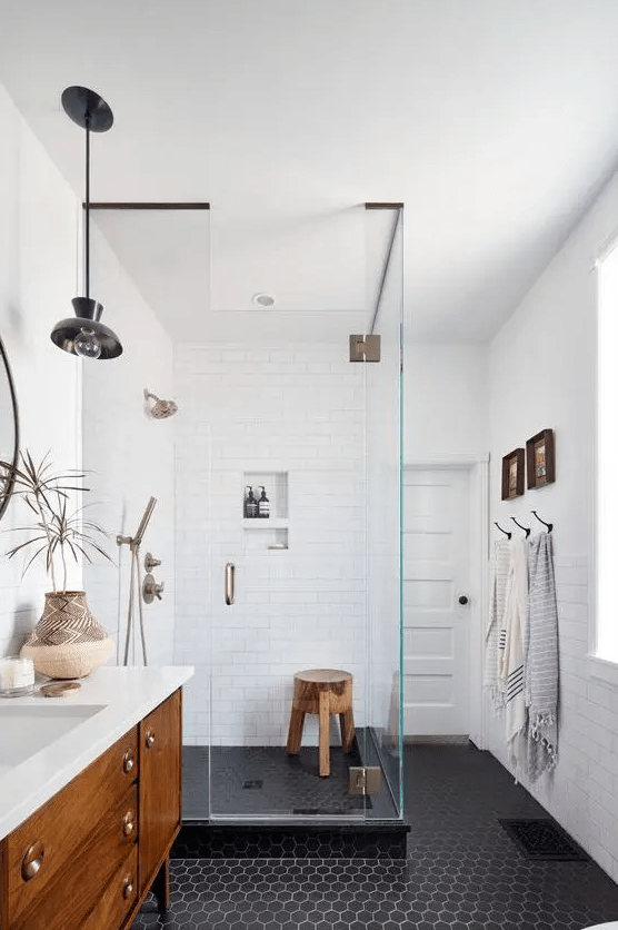 a beautiful mid-century modern bathroom with white subway and black hex tiles, a stained vanity, brass and black fixtures